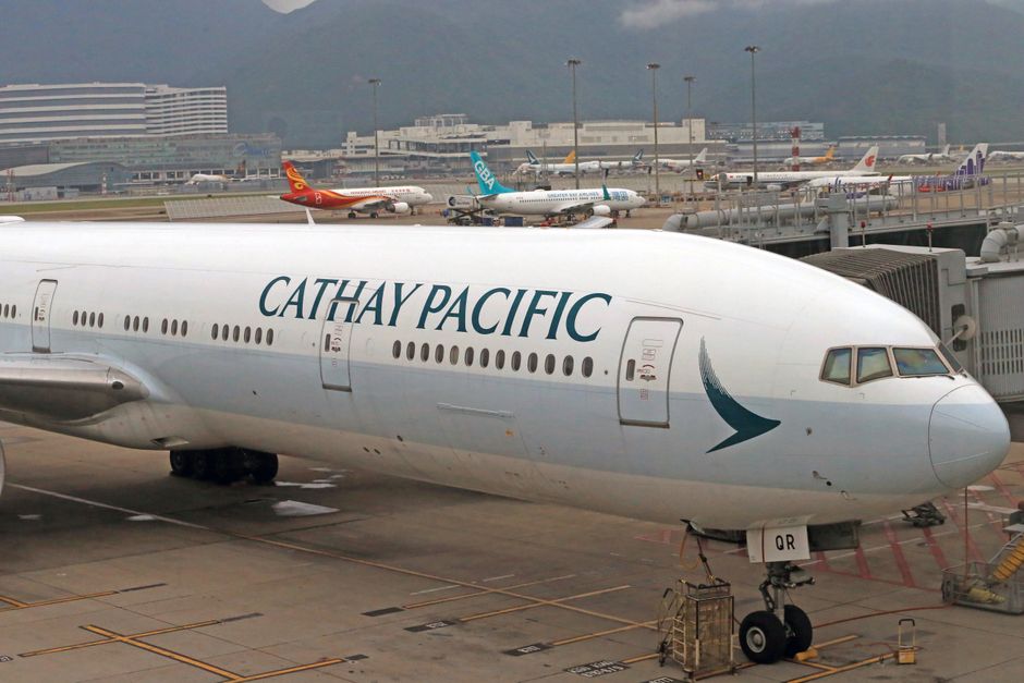 Cathay Pacific Boeing 777 aircraft parked at airport gate with terminal in the background.