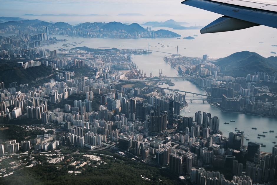 Stunning aerial view of Hong Kong cityscape with mountains and ocean in the background from airplane window.